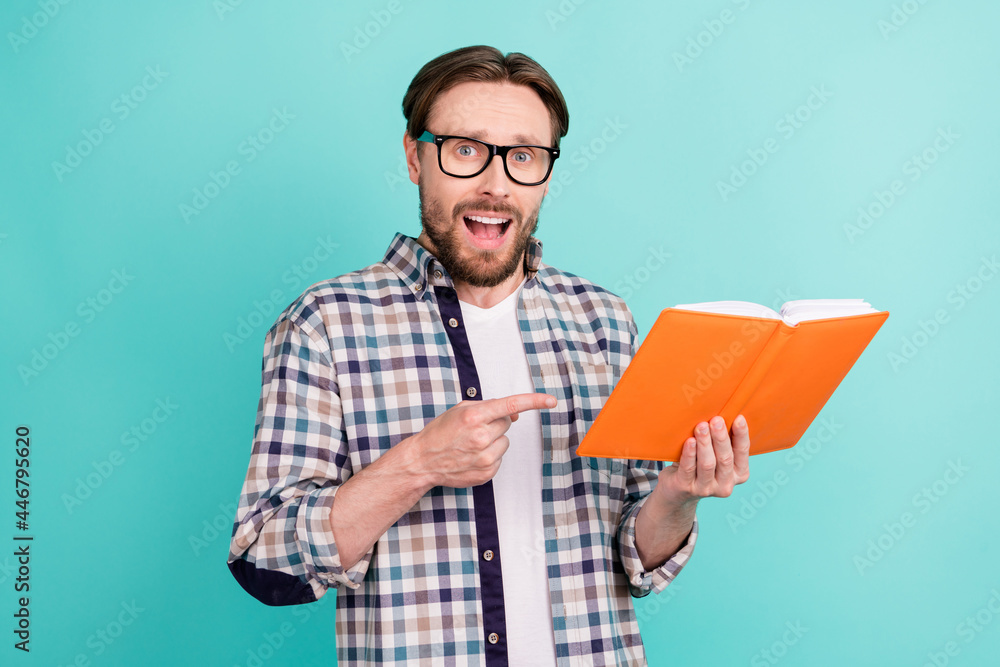 Photo of young man amazed excited point finger book education information isolated over teal color background Photo of young man amazed excited point finger book education information isolated over teal color background