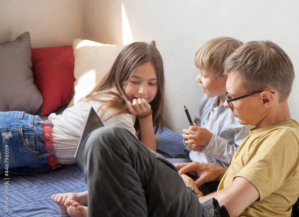 Obraz premium brother, sister and dad are sitting on the bed with a laptop and discussing. The concept of a family holiday
