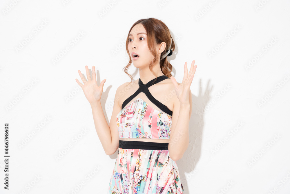 Fototapeta premium 白い壁の前に立って、胸に手を当てる、ワンピースを着た若い女性