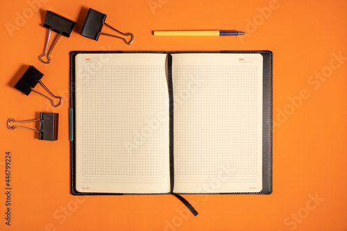 Photos Notepad and pen on an orange colored background, flat lay.