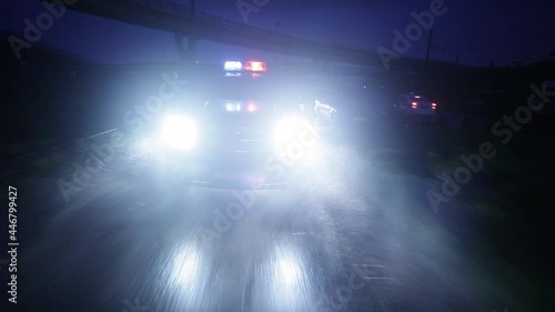 A black police car is driving fast at night with flashing lights.