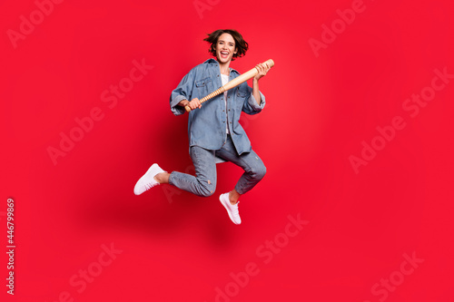 Full length photo of young woman happy positive smile hold baseball bat jump isolated over red color background