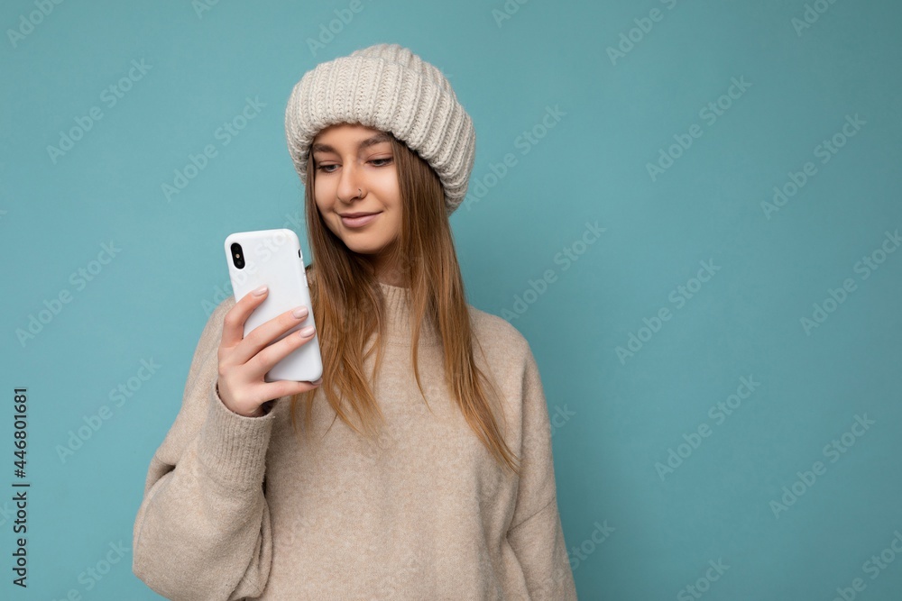 Photo shot of attractive positive good looking young woman wearing casual stylish outfit poising isolated on background with empty space holding in hand and using mobile phone messaging sms looking at Photo shot of attractive positive good looking young woman wearing casual stylish outfit poising isolated on background with empty space holding in hand and using mobile phone messaging sms looking at
