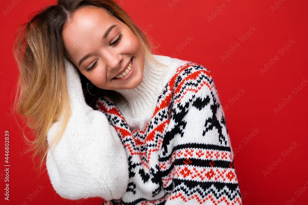 Young beautiful woman. Trendy woman in casual winter sweater. Positive female shows facial emotions. Funny model isolated on red background Young beautiful woman. Trendy woman in casual winter sweater. Positive female shows facial emotions. Funny model isolated on red background