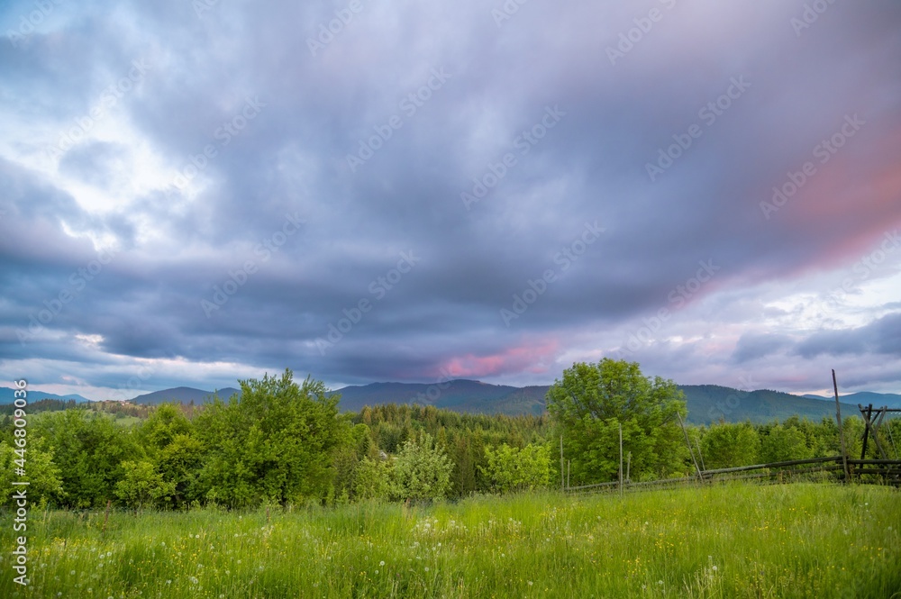 Obraz premium Evening in the mountains. Sunset. Cloudy sky of blue and pink or Very peri tones. Wooden fence. Summer time. Cloudy weather