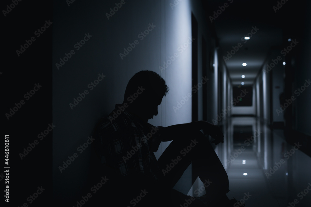 A lonely man sitting alone in hallway of an apartment building in the dark.
