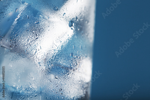 Ice cubes in a glass with refreshing ice water on a blue background.