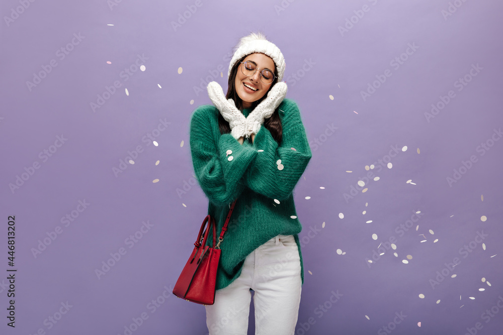 Happy woman in green woolen sweater crosses arms. Cute brunette girl in knitted hat and white pants poses with red handbag on isolated. Happy woman in green woolen sweater crosses arms. Cute brunette girl in knitted hat and white pants poses with red handbag on isolated.