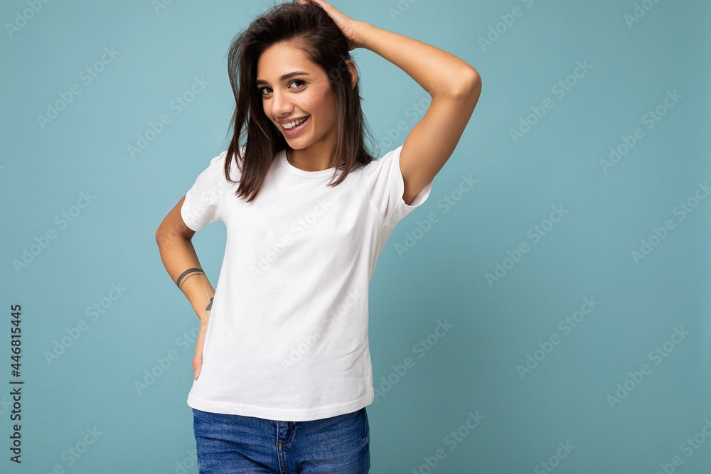 Portrait of positive cheerful fashionable smiling young brunette woman in casual white t-shirt for mockup isolated on blue background with copy space Portrait of positive cheerful fashionable smiling young brunette woman in casual white t-shirt for mockup isolated on blue background with copy space