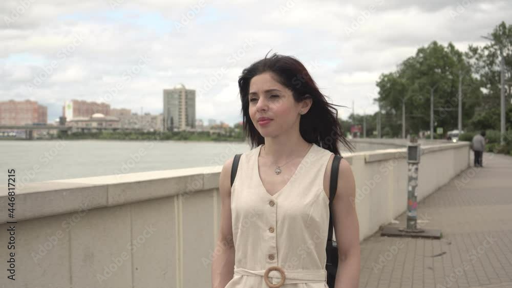 A young attractive brunette woman in a summer dress walks along the embankment of the river A young attractive brunette woman in a summer dress walks along the embankment of the river
