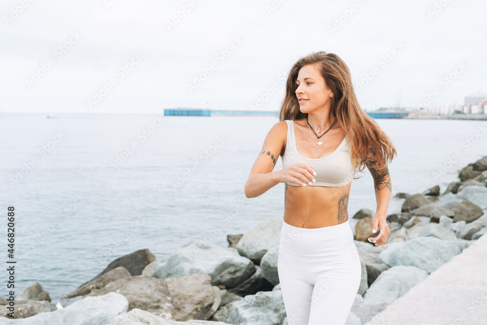 Young fit beautiful woman with long hair in white sport clothes running and enjoy life on sea beach
