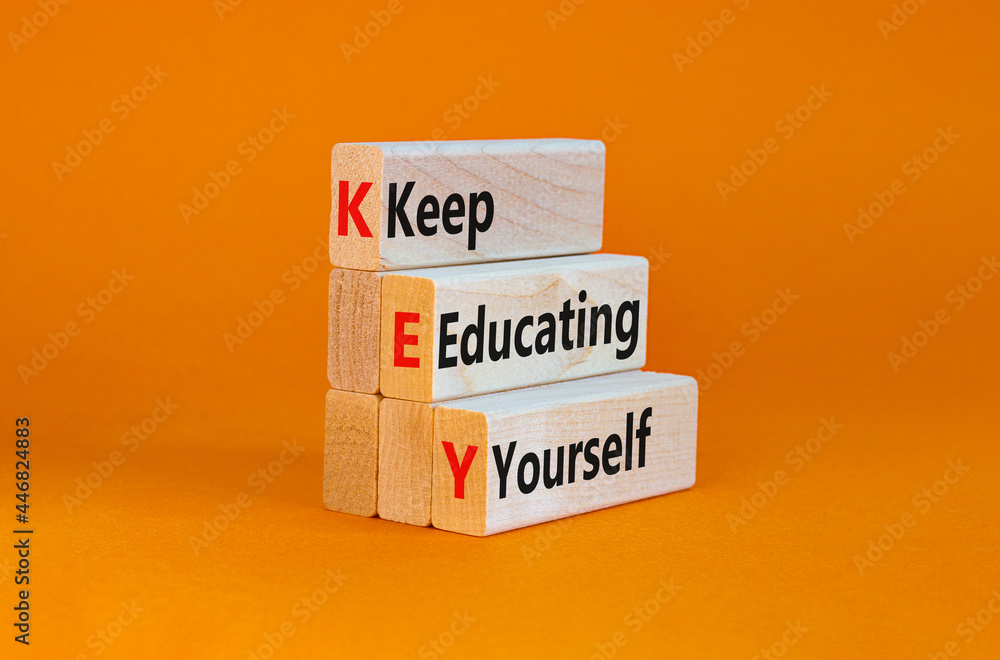 Naklejka premium KEY, keep educating yourself symbol. Wooden blocks with words 'KEY, keep educating yourself'. Beautiful orange background, copy space. Business, educational and KEY, keep educating yourself concept.