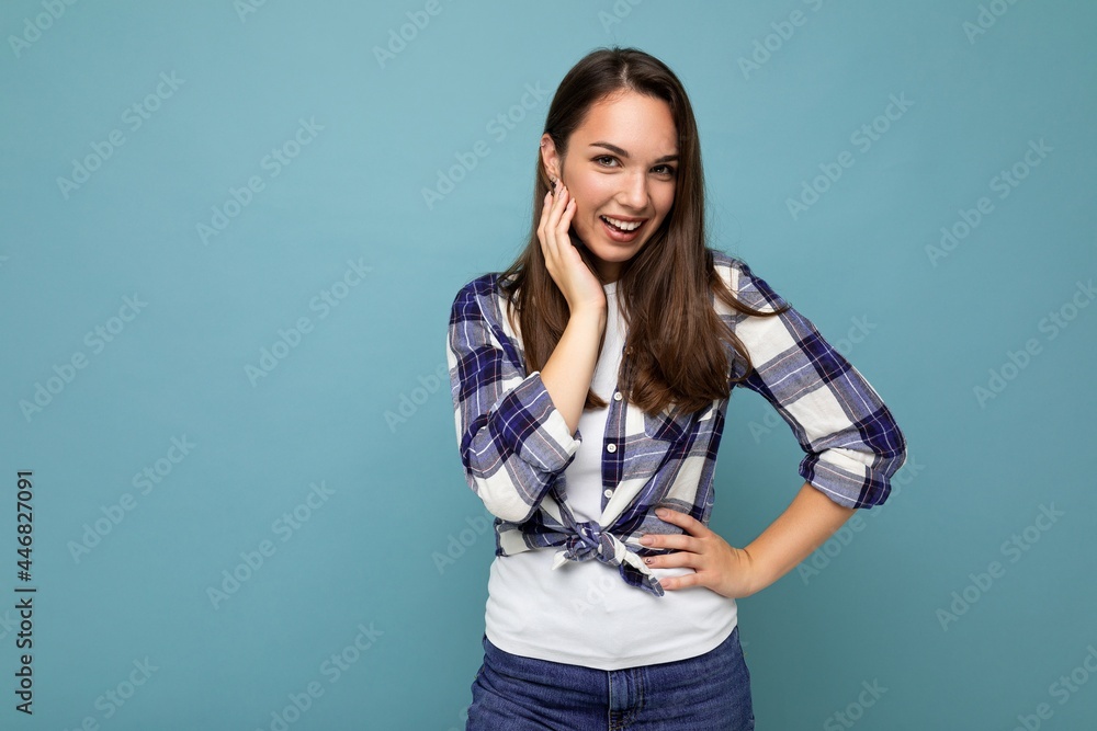 Photo portrait of young beautiful smiling hipster brunette woman in trendy blue and white shirt and jeans clothes. Sexy carefree female person posing isolated near blue wall with empty space in studio Photo portrait of young beautiful smiling hipster brunette woman in trendy blue and white shirt and jeans clothes. Sexy carefree female person posing isolated near blue wall with empty space in studio