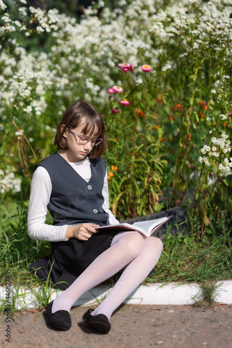 A schoolgirl sitting on the curb and reading a book on September 1
