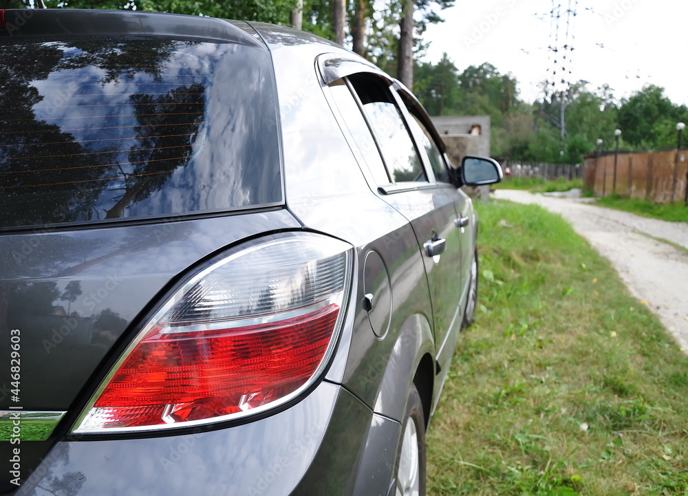 Obraz premium Rear view of the headlights of a gray car against the background of a summer road