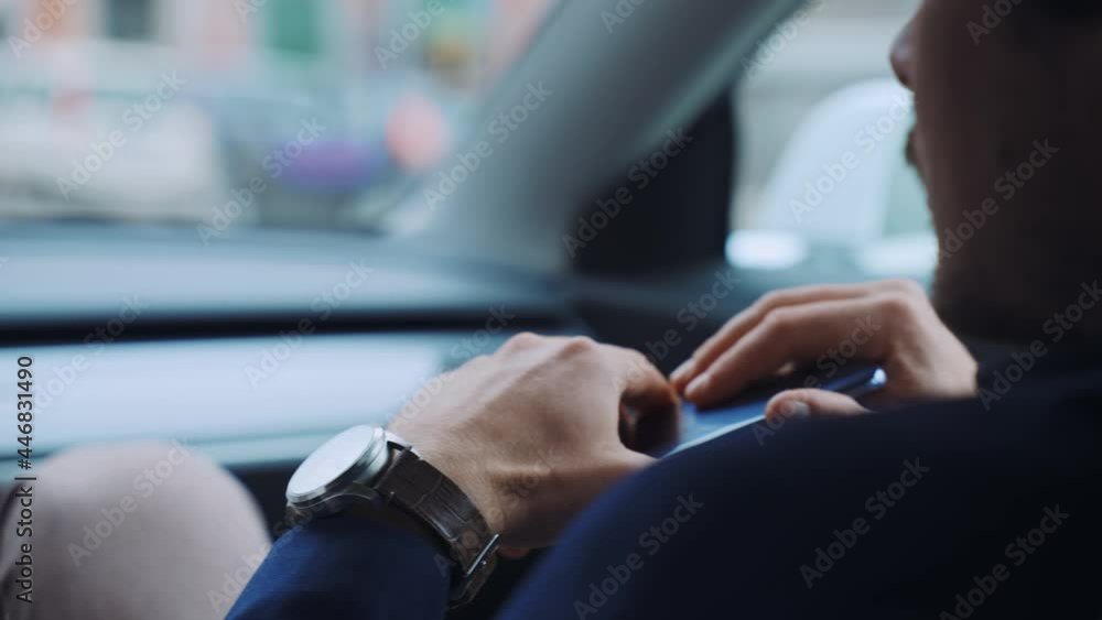 Successful businessman driving along the downtown street on high tech electric Tesla car Model 3 with driver, concentrated man holding smartphone in hands and looking on road. Autonomous car of new Successful businessman driving along the downtown street on high tech electric Tesla car Model 3 with driver, concentrated man holding smartphone in hands and looking on road. Autonomous car of new