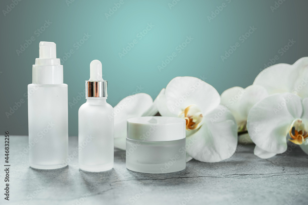 White glass serum bottle and cream jar in the bathroom with orchid flowers in the background, unbranded cosmetic products, spa cosmetic product branding mockup White glass serum bottle and cream jar in the bathroom with orchid flowers in the background, unbranded cosmetic products, spa cosmetic product branding mockup