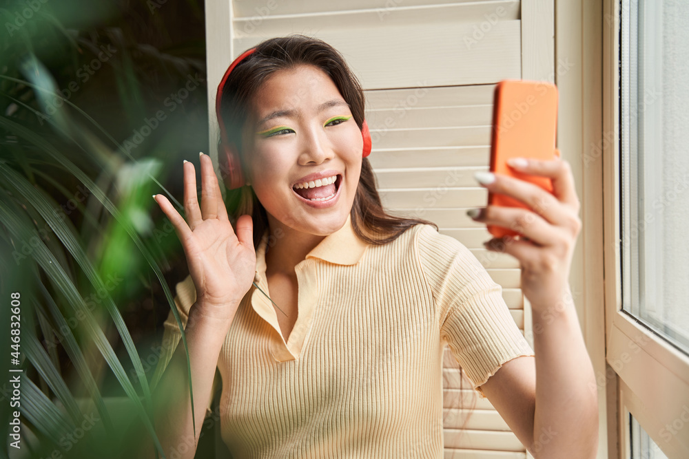 Woman wearing headphones waving to the smartphone camera while chatting Woman wearing headphones waving to the smartphone camera while chatting