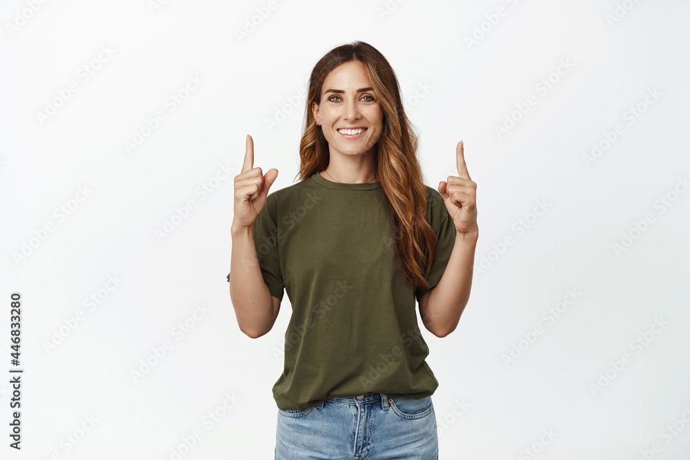 Image of caucasian smiling woman looking happy, pointing fingers up at top advertisement, showing sale, recommend store, standing against white background Image of caucasian smiling woman looking happy, pointing fingers up at top advertisement, showing sale, recommend store, standing against white background