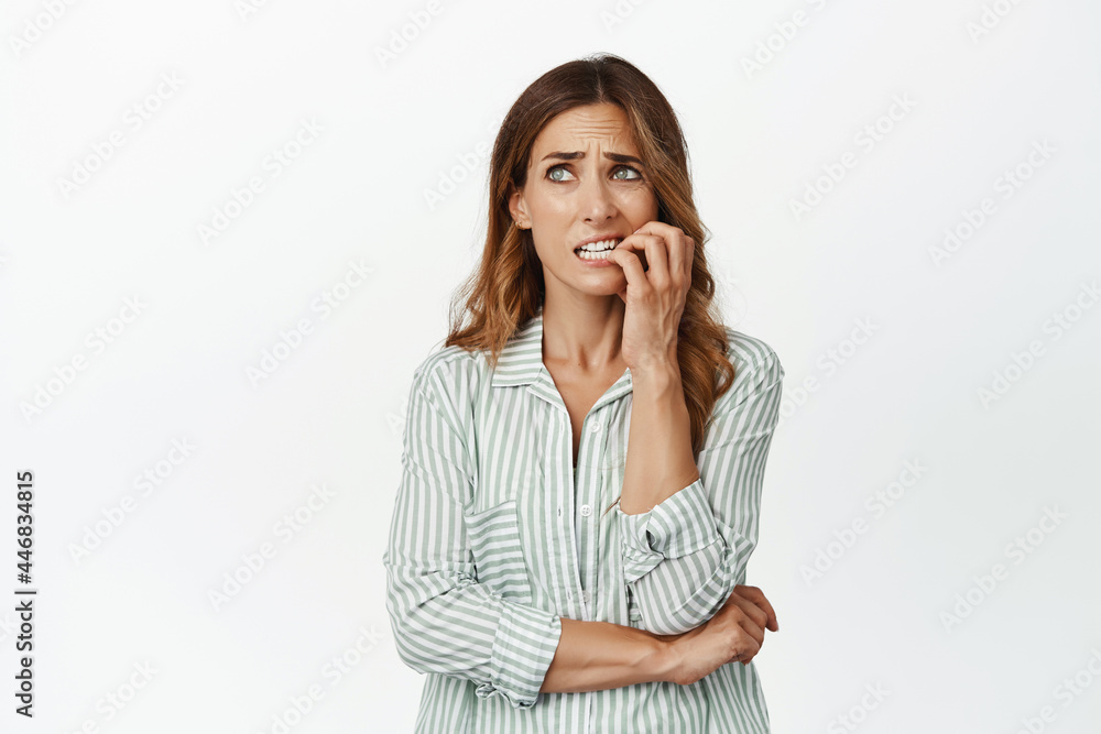Portrait of nervous brunette woman biting fingers and looking aside worried, panicking, standing alarmed, scared of smth, standing in blouse against white background Portrait of nervous brunette woman biting fingers and looking aside worried, panicking, standing alarmed, scared of smth, standing in blouse against white background