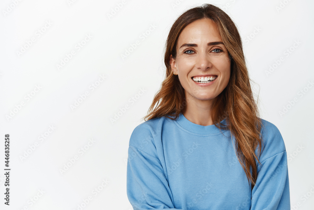 Portrait of ambitious and confident adult 30s woman, cross arms and smiling happy at camera, looking forward, standing against white background Portrait of ambitious and confident adult 30s woman, cross arms and smiling happy at camera, looking forward, standing against white background