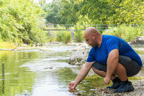 Фотография A stocky Caucasian hiker man touching the water of a river.