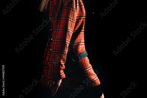 Part of a female figure wearing a checkered red jacket on black background. Runway fashion show