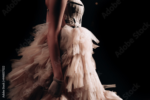 Part of a female figure dressed in a lush beige dress and a glove on her hand on black background. Runway fashion show