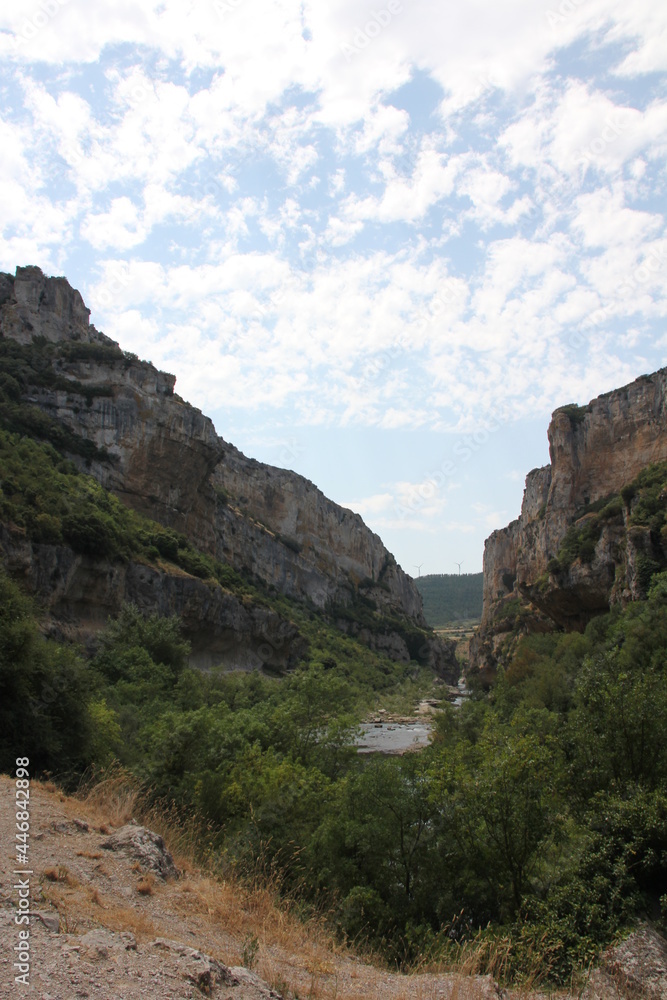 Cliffs of large rocks with vegetation and two windmills in the background at the Foz de Lumbier in Navarra