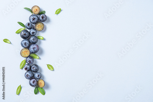 Concept flat lay with a few juicy blueberries with green leaves on blue background. Top view and copy space