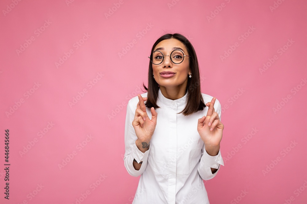 Portrait of young positive happy attractive brunette woman with sincere emotions wearing casual white shirt and optical glasses isolated over pink background with copy space and gesturing fingers Portrait of young positive happy attractive brunette woman with sincere emotions wearing casual white shirt and optical glasses isolated over pink background with copy space and gesturing fingers