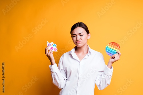 Sad Asian girl holding pop it and simple dimple in her hands, not knowing what to choose. Antistress toys