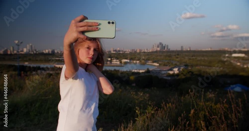 Blonde teen taking selfie in park. Closeup of teenager searching best pose for selfie portrait. Trendy girl taking selfie photo on smart phone