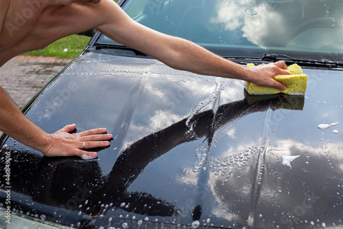 wash the hood of a black car on a sunny day in the garden after a flood,