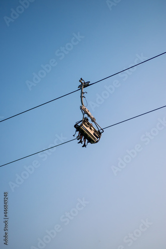 Four-seat chairlift with couple of tourist while using it seen from below against blue sky.