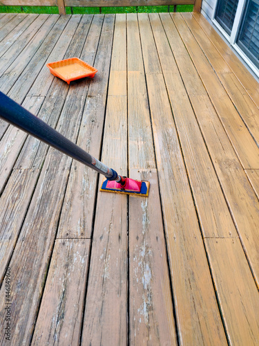 Wood stain with a paint pad on wooden deck floor.