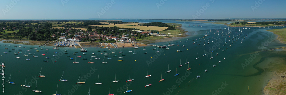 Itchenor West Sussex with sailing boats moored in the estuary and on the wooden jetty set in the beautiful countryside of Southern England. Aerial panoramiv view.