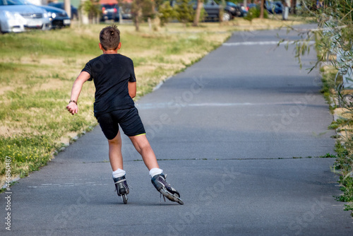 A sporting, athletic boy roller skating in a park on a summer day. © Sergei