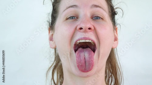 Joke and laugh. Real Caucasian woman smiling and showing tongue. Close-up frame of face on white background. Blue eyes and tousled hair in a ponytail. Happy and cheerful adult girl. raise eyebrows.