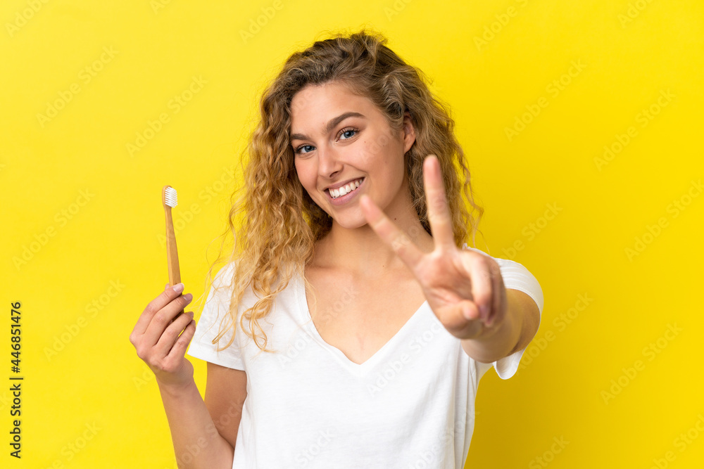 Young caucasian woman holding a brushing teeth isolated on yellow background smiling and showing victory sign Young caucasian woman holding a brushing teeth isolated on yellow background smiling and showing victory sign