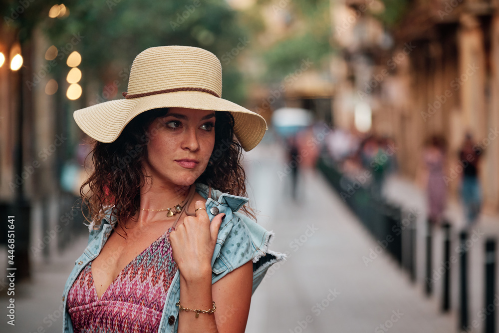 Portrait of a brunette girl with a hat and bag posing for a photoshoot on a street in the city of Barcelona.