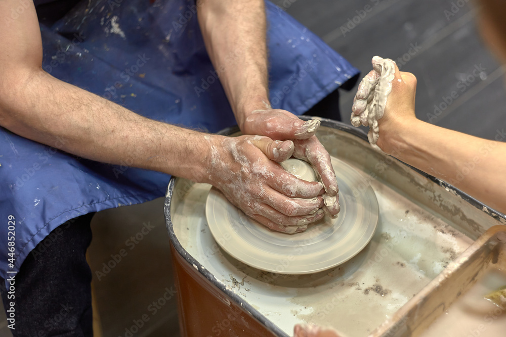 Hands of a man who learns to work with clay on potter's wheel and his ceramist teacher