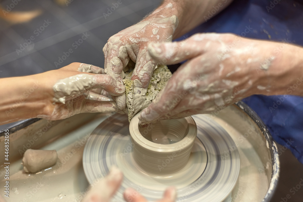 Hands of a man who learns to wipe the product with a sponge on a potter's wheel and his teacher