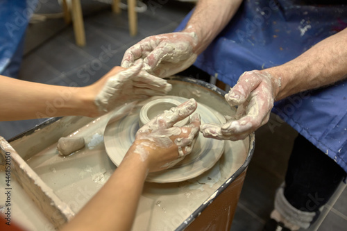 Hands of a man who learns to work with clay on potter's wheel and his ceramist teacher
