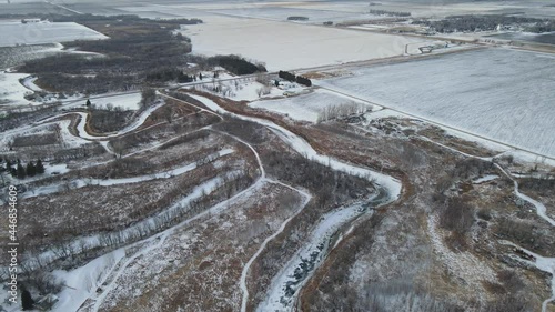 Aerial view of snowy farmlands and winding, frozen river in rural North Dakota. Winter, sunset.