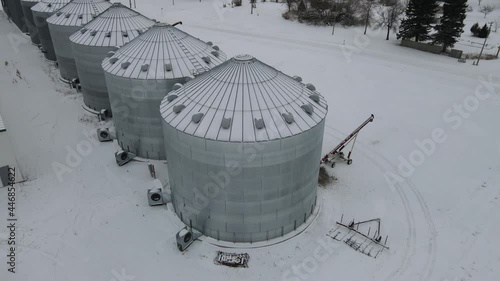 Neche, ND - 12 27 2020: Aerial clip circling multiple grey, metal agricultural grain bins. Storage silos. North Dakota, winter. photo