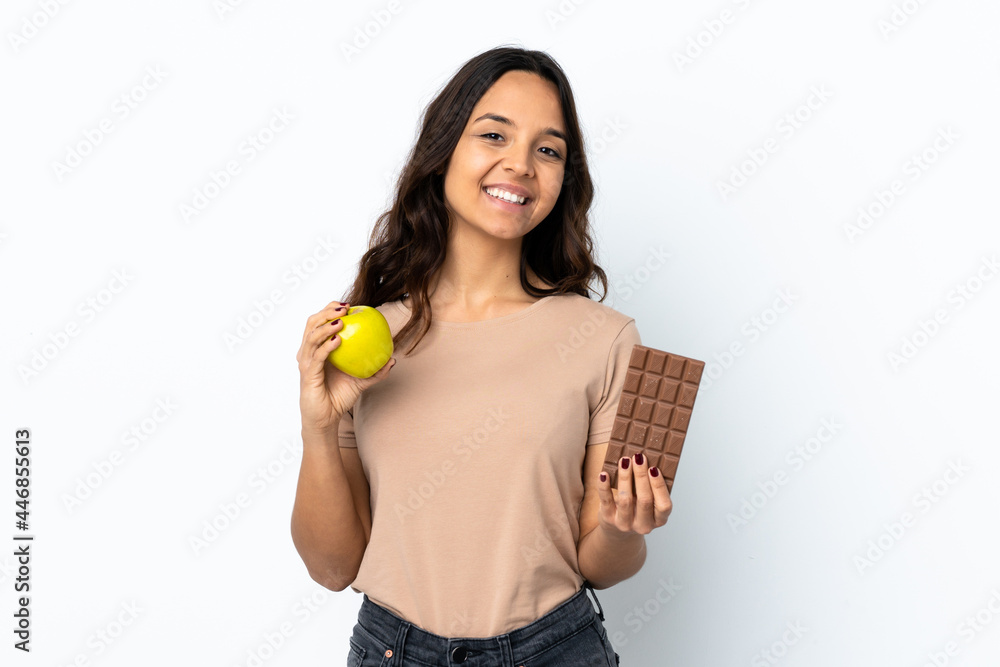 Young woman over isolated white background taking a chocolate tablet in one hand and an apple in the other Young woman over isolated white background taking a chocolate tablet in one hand and an apple in the other