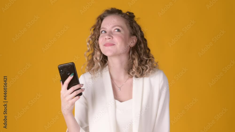 Portrait of Happy young woman girl 20s posing with phone pointing to gadget screen with index finger isolated on yellow background. People lifestyle concept Portrait of Happy young woman girl 20s posing with phone pointing to gadget screen with index finger isolated on yellow background. People lifestyle concept