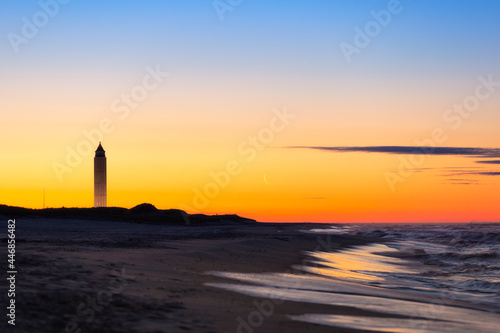 Crescent moon rising just before sunrise next to a tall tower on the beach. Jones Beach State Park, New York photo