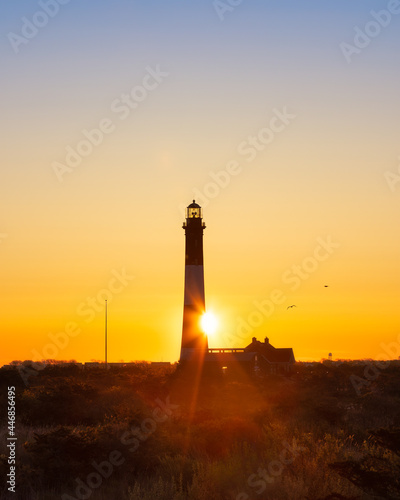 Sun rising from behind a tall lighthouse, creating a golden star burst. Fire Island, Long Island New York